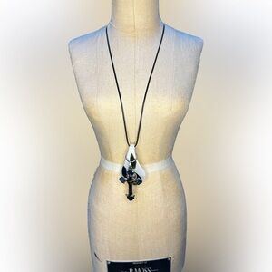 Glass pendant with ornate cross pendant in front on black rope chain.